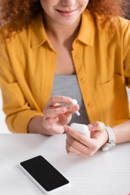 Davanın yanında kulaklık tutan genç serbest çalışan görüntüsü ve boş ekranlı akıllı telefon, bulanık arkaplan.