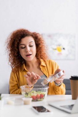 Genç serbest çalışan bulanık ön planda evde taze salata yiyor.