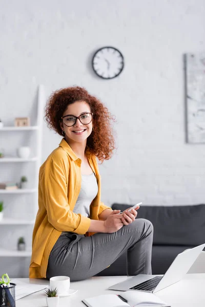 Freelance Fericit Uitându Cameră Timp Stați Birou Smartphone Lângă Laptop — Fotografie, imagine de stoc