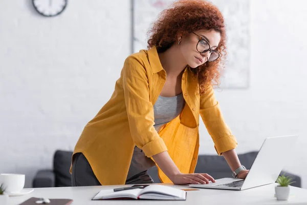 Freelance Riccio Occhiali Piedi Vicino Alla Scrivania Con Computer Portatile — Foto Stock