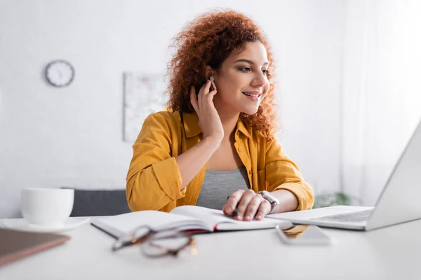 Happy Freelancer Adjusting Earphone While Sitting Laptop Blurred Foreground — Stock Photo, Image