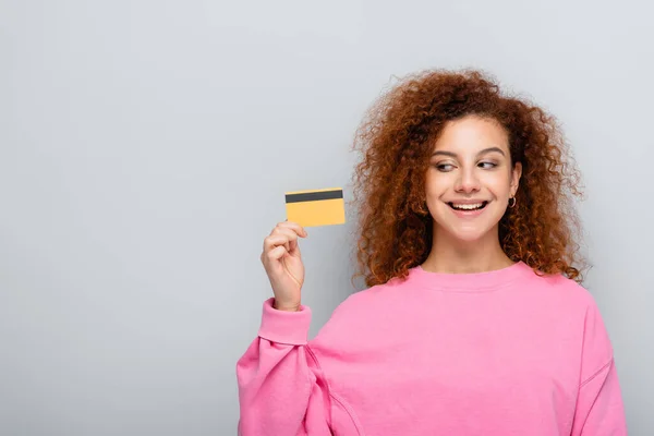 穿着粉色套头毛衣的高兴女人拿着用灰色隔开的信用卡 — 图库照片