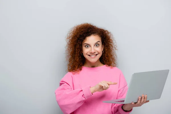 Mujer Emocionada Mirando Cámara Mientras Apunta Computadora Portátil Aislado Gris — Foto de Stock