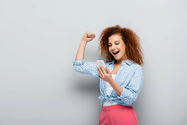 Excited Woman Showing Win Gesture While Looking Mobile Phone Grey — Stock Photo, Image