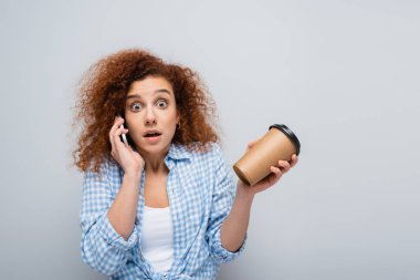 Gri bardakta kağıt bardak tutan bir kadın cep telefonundan arıyor.