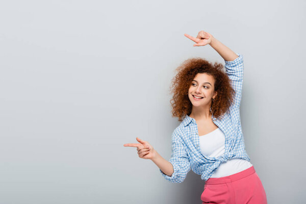 веселая женщина смотрит в сторону и указывает пальцами на сером фоне