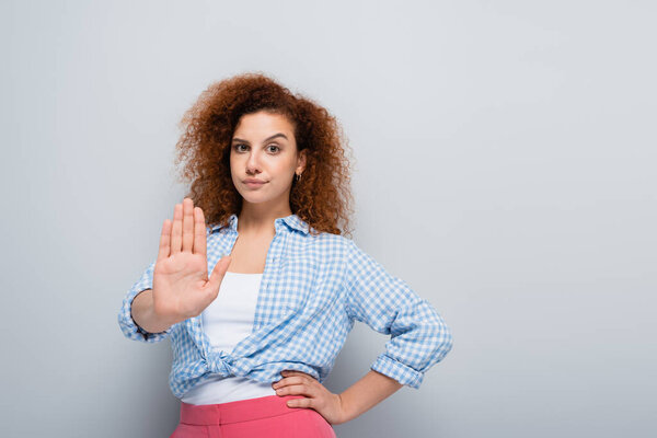 displeased woman showing refuse gesture while standing with hand on hip on grey background