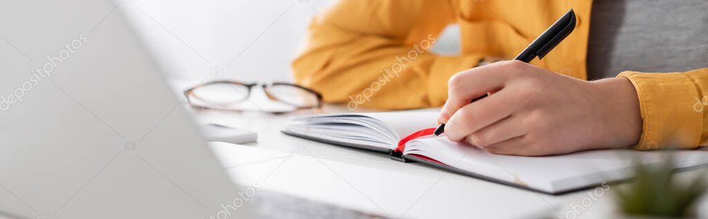 partial view of freelancer writing in notebook on blurred foreground, banner