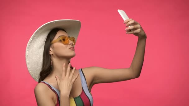 Γυναίκα Καπέλο Και Γυαλιά Ηλίου Που Έχουν Βιντεοκλήση Απομονωμένη Ροζ — Αρχείο Βίντεο