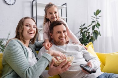 Gülümseyen adam uzaktan kumanda ve aile yanında patlamış mısır tutuyor. 