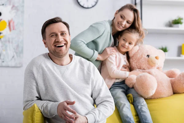 Cheerful Man Looking Camera Blurred Wife Daughter Soft Toy — Stock Photo, Image