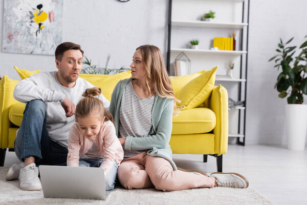Child using laptop near excited parents on floor at home 