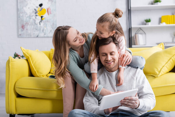 Smiling woman looking at daughter hugging father with digital tablet 