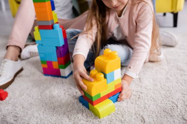 Annesinin yanında halıda oynayan çocuk manzarası. 