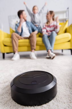 Halıda robotik süpürge, bulanık arka planda aile yakınları. 