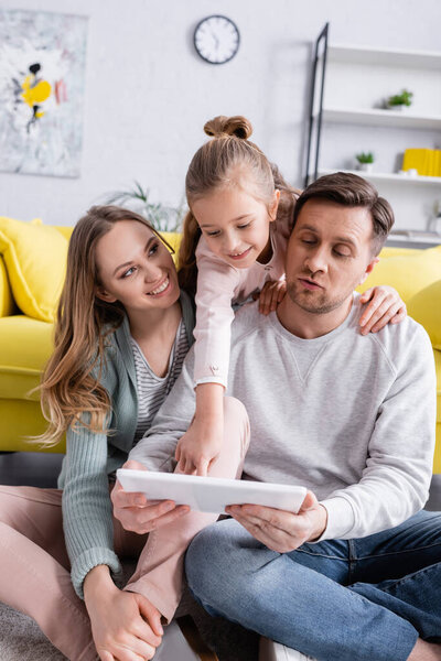 Happy child using digital tablet near parents on floor in living room 