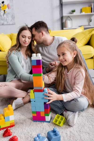 快乐的女孩在客厅的父母身边玩着五彩缤纷的积木 — 图库照片