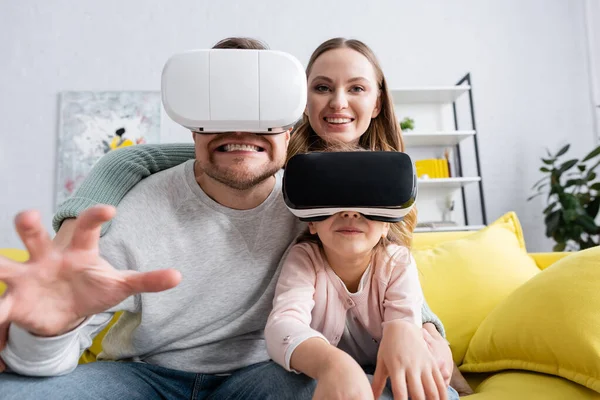 Kid and father gaming in vr headsets near smiling mom at home