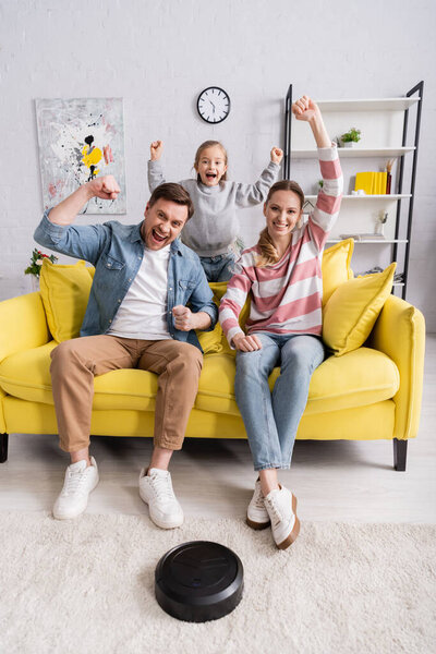Excited family looking at camera near robotic vacuum cleaner at home 