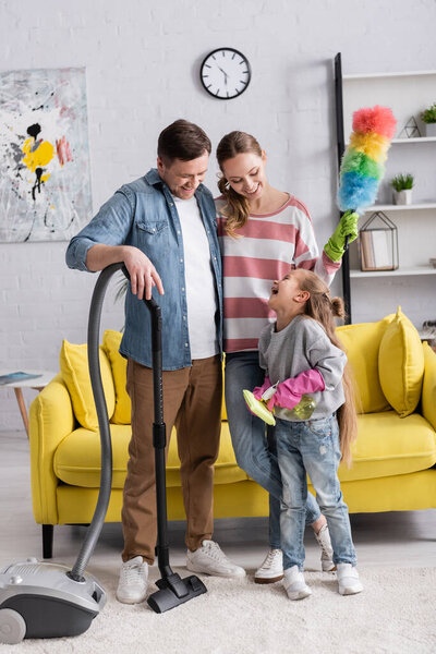 Smiling parents looking at daughter with detergent and rag at home 