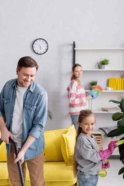 Smiling Father Holding Vacuum Cleaner Daughter Cleaning Plant Wife Home — Stock Photo, Image