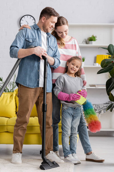 Smiling family with cleaning supplies standing in living room 