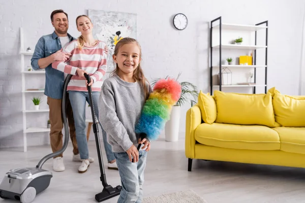 快乐的孩子抱着灰尘刷子靠近妈妈 带着吸尘器 爸爸在家里 — 图库照片