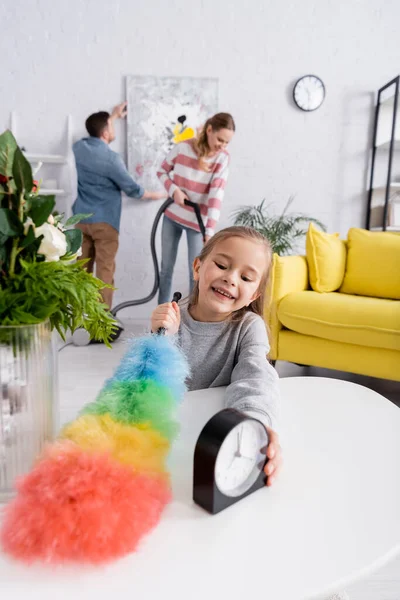 Kid Trzyma Szczotkę Kurzu Stół Podczas Gdy Rodzice Sprzątają Salon — Zdjęcie stockowe