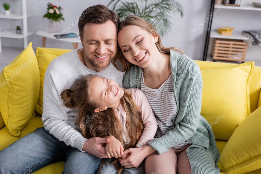 Happy family with closed eyes hugging on couch