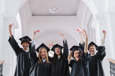 Heyecanlı çok kültürlü öğrenciler ve evet işareti gösteren diplomalar. 