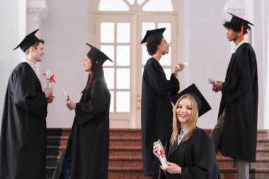 Diplomalı, gülümseyen bekar, çok ırklı arkadaşlarının yanında kameraya bakıyor. 