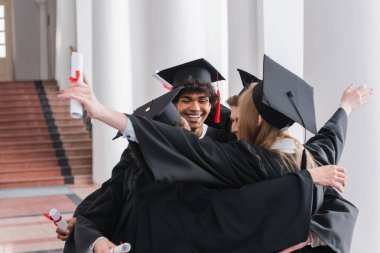 Gülümseyen Afro-Amerikan mezunları diploma kucaklayan arkadaşlarıyla 