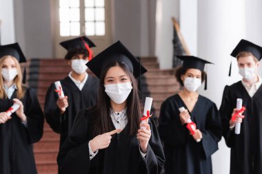 Tıp maskeli bir Asyalı diplomayı kurdeleyle işaret ediyor. 