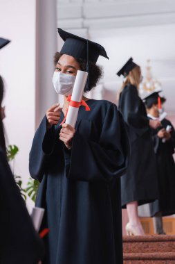 Tıp maskeli Afrikalı Amerikalı öğrenci diplomayı işaret ediyor. 