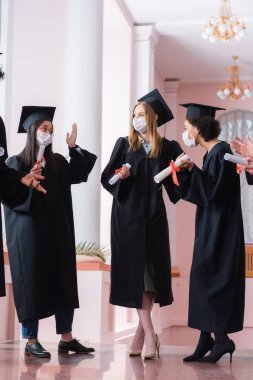 Tıp maskeli, diplomalı ve üniversite koridorunda konuşan çok ırklı mezunlar. 