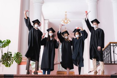 Tıp maskesi takan çok ırklı mezunlar üniversitede yükselen diplomalar 