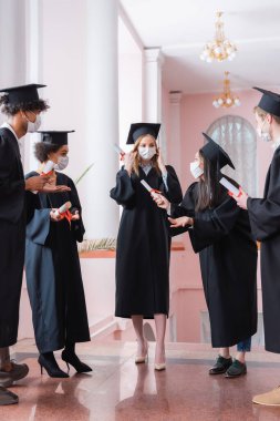 Koruyucu maskeli Asyalı bekar, çok ırklı arkadaşlarının yanında diploma taşıyor. 