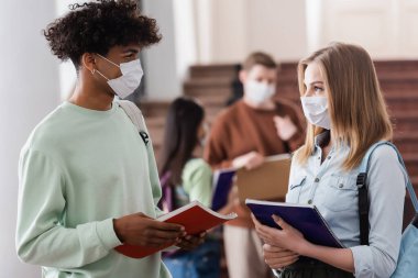 Tıp maskeli çok ırklı öğrenciler üniversitede defter tutuyorlar. 