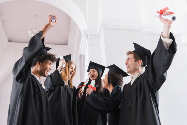 Cheerful multiethnic graduates with diplomas in university 