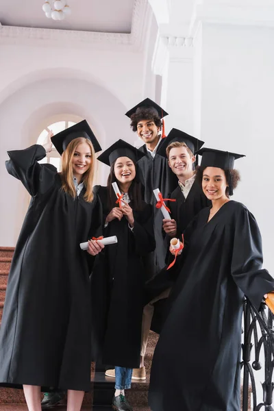 Graduados Multiculturais Sorridentes Vestidos Acadêmicos Detentores Diplomas — Fotografia de Stock