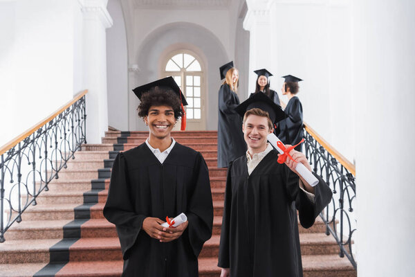 Positive interracial students holding diplomas in university 