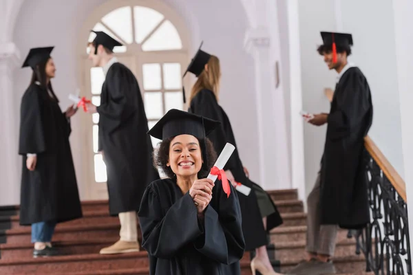 Feliz Afroamericano Graduado Sosteniendo Diploma Cerca Borrosa Amigos Universidad —  Fotos de Stock