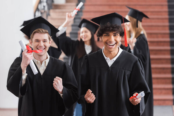 African american bachelor showing yes gesture near friend with diploma  