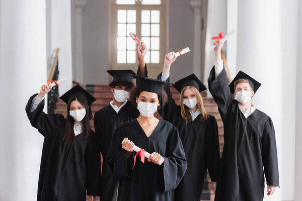 Interracial bachelors in protective masks holding diplomas 