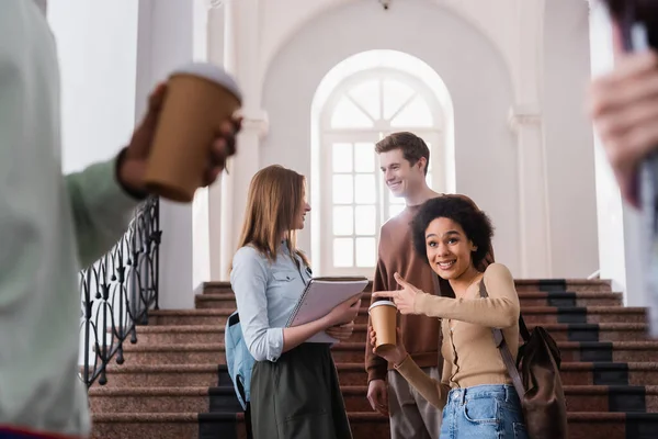 アフリカ系アメリカ人の学生を笑顔でコーヒーを飲みながら大学の友達を指差して — ストック写真