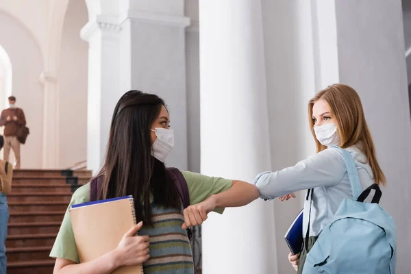 Estudiantes Multiétnicos Con Máscaras Protectoras Sosteniendo Cuadernos Saludos Salón Universitario —  Fotos de Stock