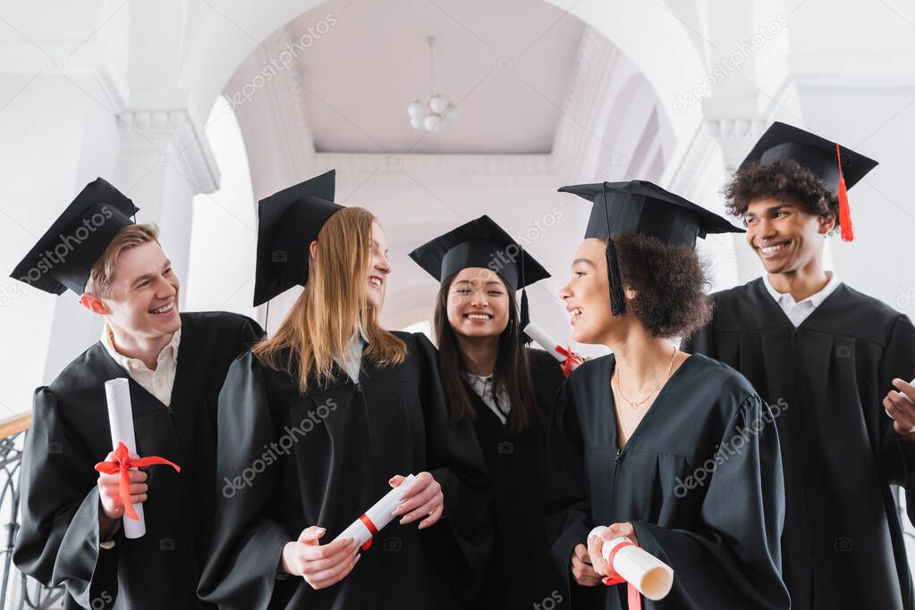 Smiling interracial graduates looking at each other in university 