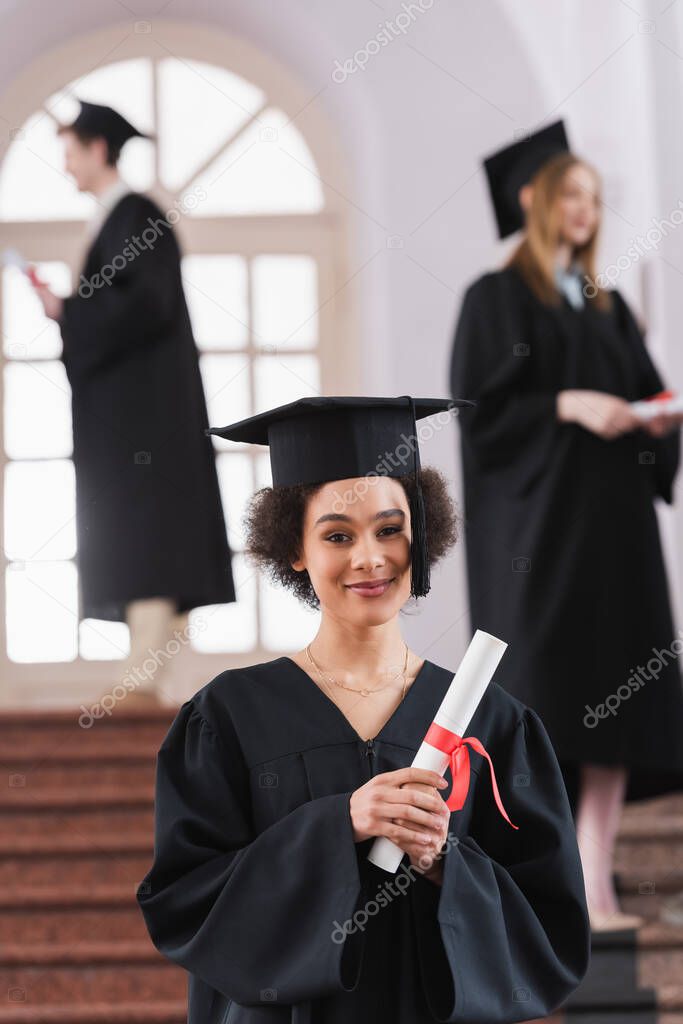 African american graduate holding diploma and looking at camera in university 