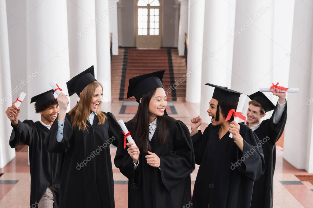 Excited interracial graduates holding diplomas in university 