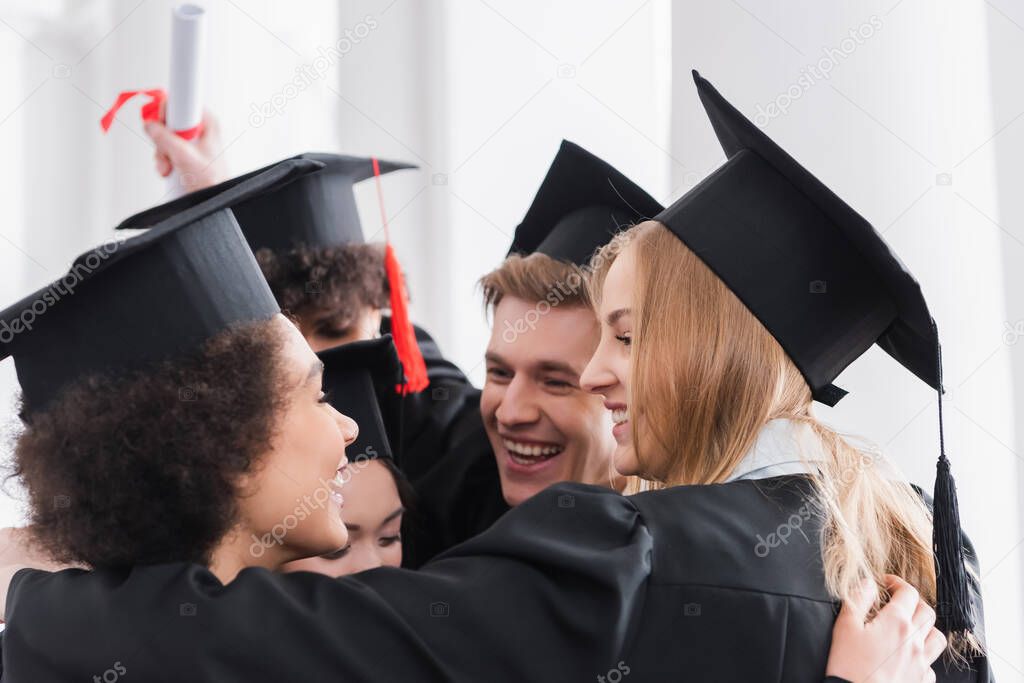 Smiling multiethnic students in caps hugging in university 